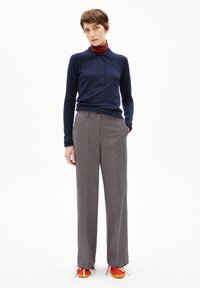 Marineblaues Langarm-Polo mit Knopfleiste, kombiniert mit grauen weiten Hosen und roten Sneakers, ergänzt durch einen gestreiften roten und marineblauen Schal.