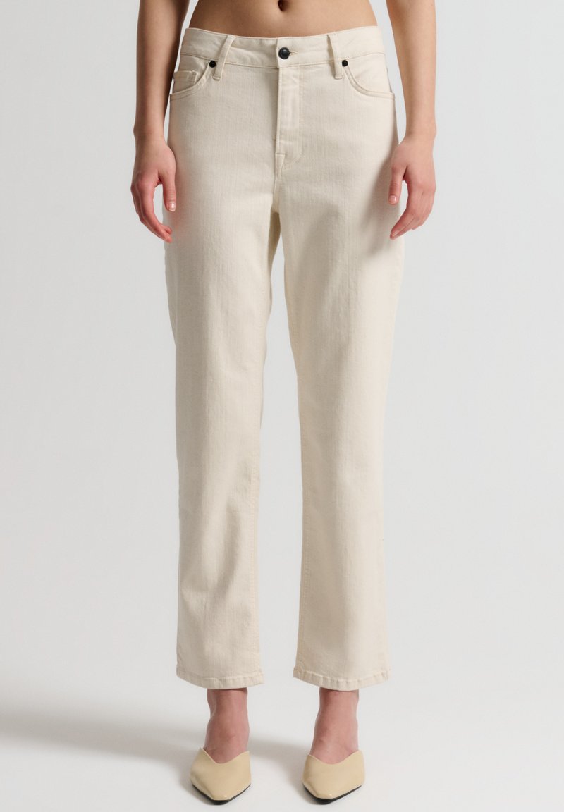 Pantaloni in denim beige con vestibilità a gamba dritta, design a cinque tasche e chiusura con bottone. Il tessuto appare testurizzato, con dettagli di cucitura discreti.