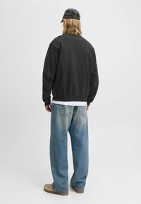 Sort sweatshirt med rund hals, løs pasform, ribbede manchetter, parret med falmede blå vidde jeans og beige slip-on sko.