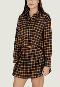 Camicia corta a quadri marrone con chiusura a bottoni abbinata a una gonna plissettata coordinata. Entrambi realizzati in tessuto con una morbida texture.