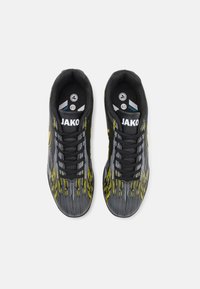 Zapatos deportivos en negro y gris con detalles en amarillo, que presentan una parte superior texturizada, seis ojetes y un logotipo prominente en la lengua.