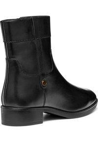 Botte de cheville en cuir noir avec un bout arrondi, un petit talon et des coutures latérales. Présente un accent de bouton près du haut et une finition lisse.