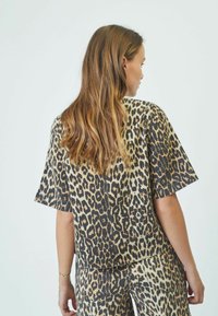 Top a maniche corte con stampa leopardata realizzato in tessuto morbido, con una vestibilità comoda e orlo arrotondato. Il design presenta diverse tonalità di macchie marroni e nere.