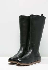 Botas de cuero negro hasta la rodilla con un acabado suave, puntera redonda y suela de goma. Con tira en la parte posterior y un ligero detalle de costura.