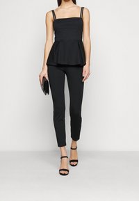 Svart peplumtop med justerbara band som har dekorativa detaljer, ihop med svarta tajta byxor och klackskor med remmar, vilket skapar en strömlinjeformad silhuett.