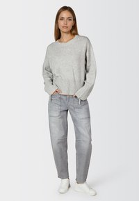 Hellgrauer, gestrickter Pullover mit geripptem Saum und Bündchen, kombiniert mit hellgrauen, locker sitzenden Jeans und weißen Sneakers.