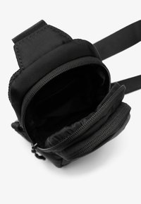 Borsa nera in nylon con superficie texturizzata, dotata di scomparto principale con zip e tasca aggiuntiva, tracolla regolabile e design arrotondato.
