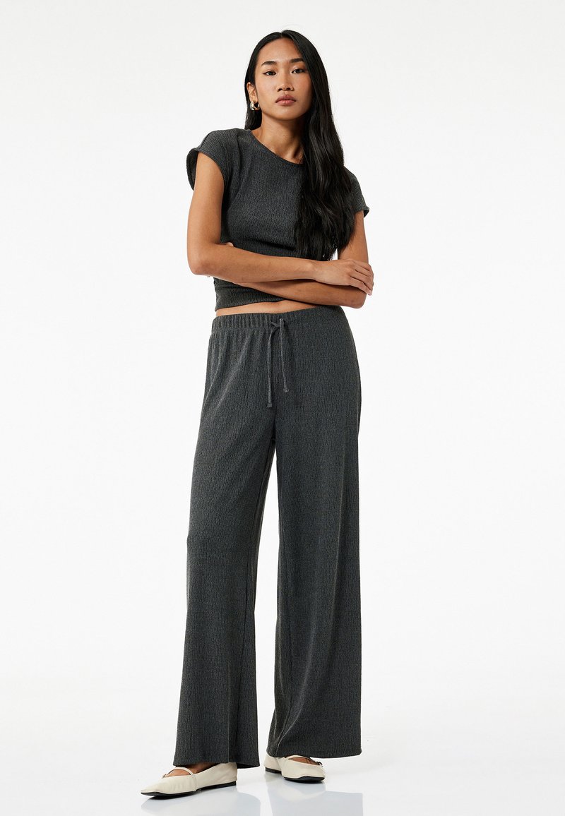 Grijs geribbeld tweedelig tenue met een aansluitend top met korte mouwen en losse, wijde broek met een trekkoord in de taille.