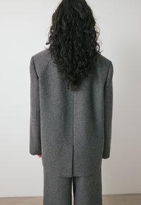 Sivša krojena blazer iz teksturirane tkanine, s strukturiranimi rameni, enim zadnjim razporkom in usklajenimi hlačami.