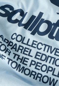 T-shirt en coton bleu clair avec du texte bleu foncé. Le texte comprend "sculpt", "ÉDITION VÊTEMENTS COLLECTIVE" et "POUR LE PEUPLE DE DEMAIN".