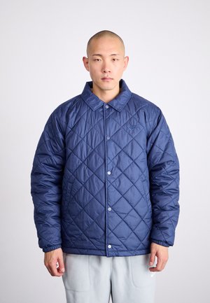 Marineblau gesteppte Jacke mit Kragen, Druckknöpfen und elastischen Bündchen. Verfügt über ein kleines Logo auf der Brust, gefertigt aus einem glänzenden Material.