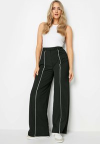 Musta leveälahkeinen housut valkoisella vetoketjulla edessä, korkea vyötärö ja pehmeä kangas, yhdistetty valkoisen hihattoman topin kanssa.