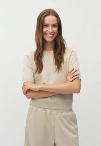 Beige gestricktes Kurzarmoberteil mit einem gerippten Rundhalsausschnitt und entspannter Passform, kombiniert mit hellbeigen, locker sitzenden Hosen.