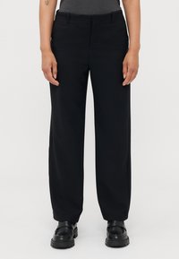 Svarte vide bukser med en glatt tekstur, med foran lommer og en klassisk linning. Kombinert med svarte loafers.