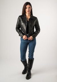 Zwarte leren jasje met een kraagontwerp, aansluitende snit en ritssluiting, gecombineerd met blauwe jeans en kniehoge zwarte laarzen.