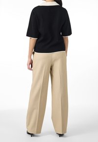 Czarna bluzka z krótkim rękawem i białym kołnierzykiem, zestawiona z beżowymi spodniami o szerokich nogawkach. Gładka faktura, dopasowany krój i klasyczny design.