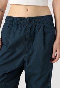 Pantaloni navy blu dalla vestibilità rilassata realizzati in tessuto leggero, con vita elastica, chiusura a bottone e tasche laterali.