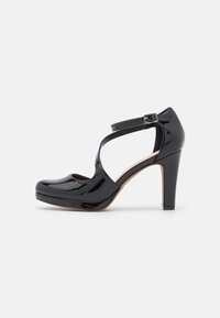 Chaussure à talons hauts en cuir verni noir avec un bout rond, un design de bride croisée et un accent de boucle. Présente une plateforme pour une hauteur supplémentaire.