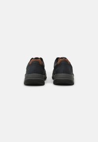 Black athletic shoes with a textured upper, brown leather accents, cushioned soles, and a sleek rounded shape.