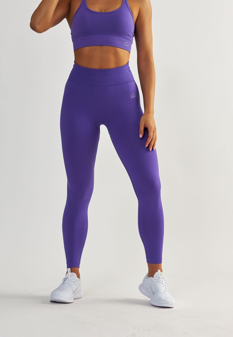 Leggings violets taille haute en matériau extensible, avec une texture lisse et un petit logo près de la taille.