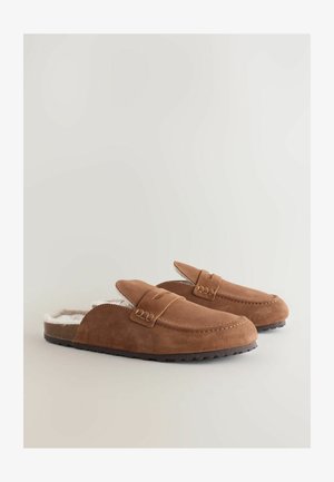 Brune ruskind slip-on tøfler med hvid kunstpelsforing, buet tådesign og dekorativ syning. Tekstureret gummi ydersål for godt greb.