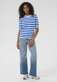 Blauw-wit gestreept T-shirt met korte mouwen, gecombineerd met lichtblauwe wijde spijkerbroek en grijze sneakers, gedragen door een model met krullend haar.