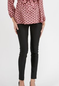 Rödkemisk mönstrad blus med långa ärmar och en rosett vid midjan, tillsammans med svarta slim-fit byxor.