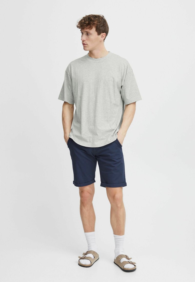 Lys grå kortærmet T-shirt parret med marineblå shorts, opslået kant, og tan sandaler med dobbelt stropper. Strømperne er hvide og ankellange.