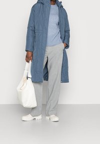 Abrigo azul acolchado con capucha, suéter de canalé azul claro, pantalones de cuadros grises, bolso blanco y zapatos de goma blancos.