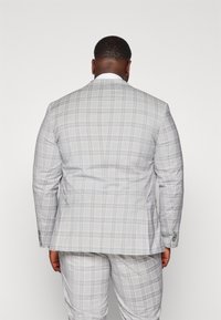 Traje de cuadros gris, con una tela texturizada y acentos en azul claro y amarillo, diseño de un solo botón con dos botones, y pantalones a juego.