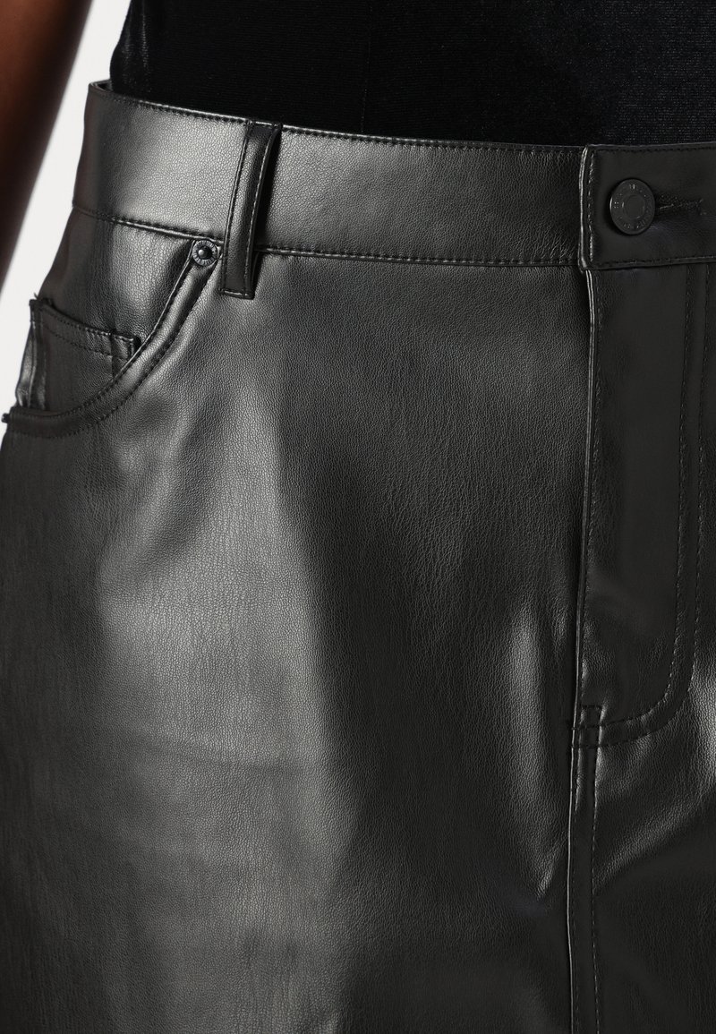 Falda de cuero negro con una textura suave, que presenta una cintura clásica, bolsillos frontales y detalles de costura.