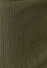 Olivengroen stof met een getextureerd geribd patroon met verhoogde, golvende lijnen. Materiaal lijkt zacht en rekbaar te zijn.