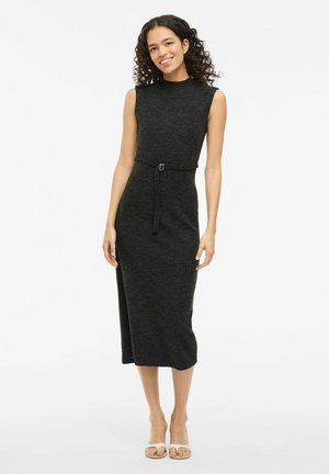 Sleeveless dark gray knit dress with a mock neck, belted waist, side slit, and fitted silhouette; worn with light-colored open-toe sandals.