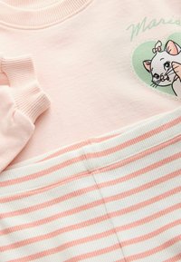 Hanorac roz cu manșete cu nervuri, având un grafic cu o pisică de desen animat și un contur de inimă verde. Asortat cu pantaloni cu nervuri în dungi albe și roz.