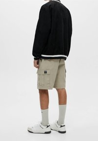 Black suede jacket with white stripe at the hem, khaki cargo shorts with pockets, white sneakers, and light grey socks.