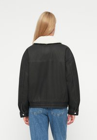 Μαύρο μπουφάν με κολάρο από γούνα, με ριμπ ύφος στον ίσιο και στις μανσέτες, με τόνους ραφής. Φορώντας με ξεθωριασμένο μπλε τζιν,