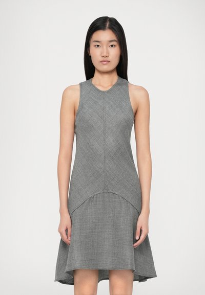 Young woman with straight black hair wearing a sleeveless, gray high-low dress with a textured fabric pattern.