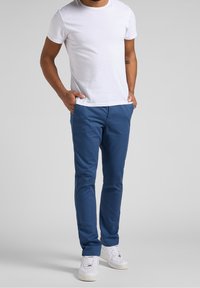 Modré chinos kalhoty s úzkým střihem, vyrobené z lehké látky. Kombinovány s jednoduchým bílým tričkem a bílými teniskami, které mají neformální design.