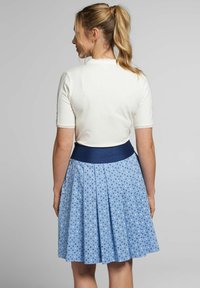 Weißes kurzärmliges Oberteil mit Spitzenbesatz, kombiniert mit einem gefalteten blauen Rock mit weißem Muster und einem marineblauen Bund.