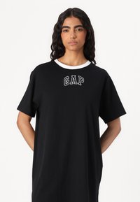 Črna majica obleka s belim okroglim izrezom, ki vsebuje izvezeno ''GAP'' logo na prsih. Ohlapna silhueta in kratki rokavi, izdelana iz mehke tkanine.