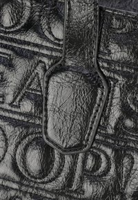 Borsa a mano in pelle nera testurizzata con lettering impresso, manici resistenti e finitura lucida. Cuciture dettagliate lungo i bordi.