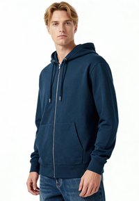 Felpa blu navy con zip in morbido tessuto, caratterizzata da una tasca frontale, coulisse e polsini a costine. Abbinata a jeans azzurri.
