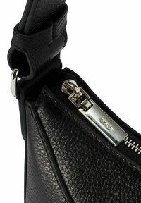 Róg czarnej torby ze skóry teksturowanej z srebrnym zamkiem i grawerowanym uchwytem, z widocznym wyszywanym paskiem i metalowym zaczepem.