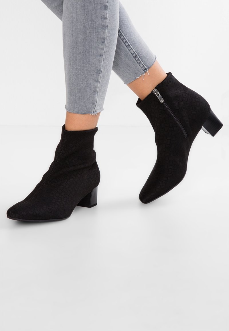 Bottines noires texturées à talons blocs et zips latéraux portées avec un jean skinny court gris clair, jambes croisées.