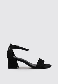 Sandalias de tacón de ante negro con una tira ancha sobre el dedo del pie y una correa en el tobillo. Tacón grueso con un acento circular en el lado exterior.