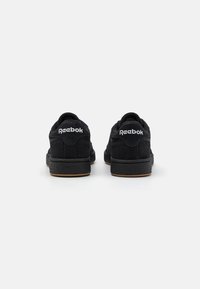 Černé semišové tenisky s texturovanou černou gumovou podrážkou. Na patě se nachází bílé logo "Reebok" a mají nízký střih.