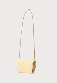 Kvadrāts dzeltenas ādas crossbody soma ar zelta ķēdes siksnu un salocītu vāku. Iezīmējas ar chevron rakstu un logotipa detaļām.