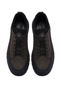 Une paire de baskets décontractées de couleur marron foncé et noire, avec des lacets noirs, des semelles épaisses et des étiquettes hexagonales de marque sur la languette, vue de dessus.