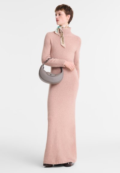 Long, pale pink knitted dress with high neck and ribbed cuffs. Accessories include a patterned scarf and a gray handbag with a curved design.