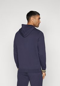 Felpa con cappuccio blu navy dalla texture liscia e polsini a coste con strisce gialle. Taglio in vita con una vestibilità morbida.